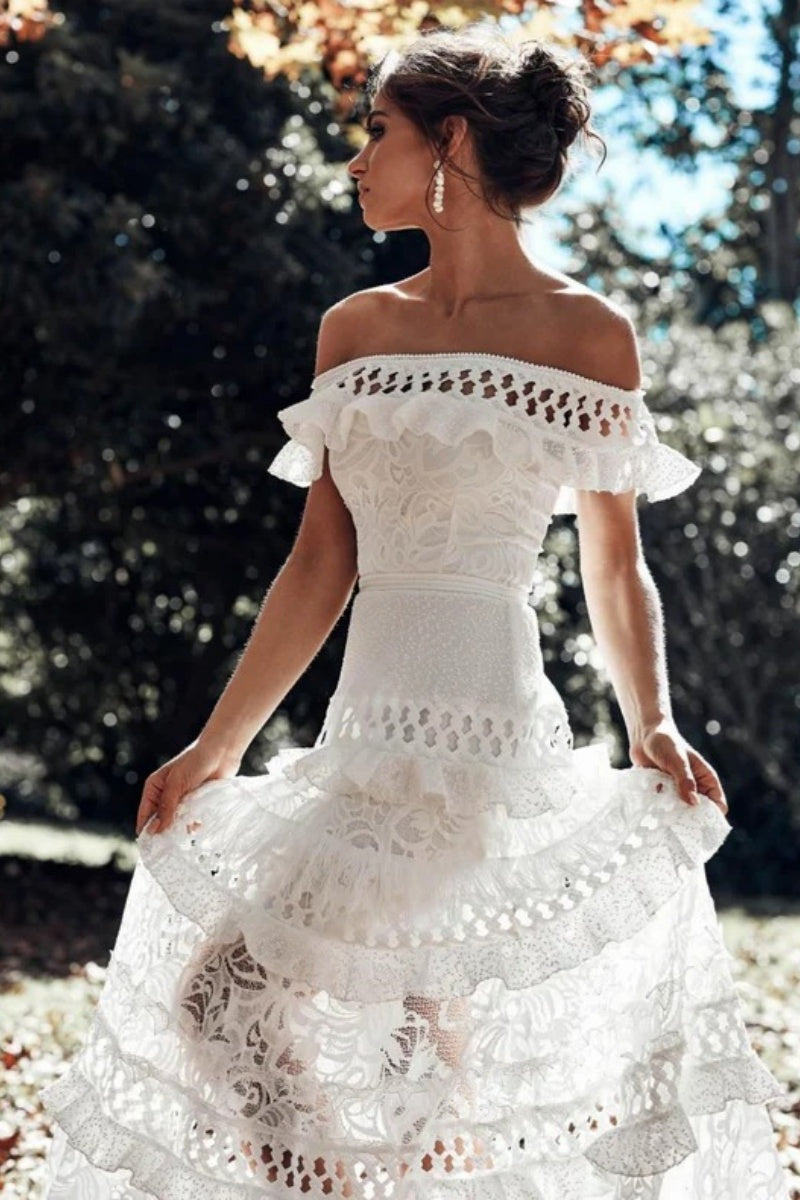 White - Woman wearing a white, off-the-shoulder maxi dress with tiered ruffles, lace, and broderie anglaise detailing.