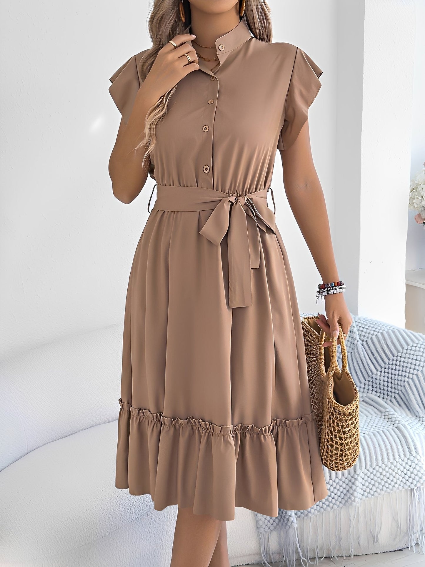 Khaki - A woman wearing a woven short-sleeve midi shirt dress with a collared neckline, button-down front, tie waist, and tiered ruffle hem, holding a woven bag.