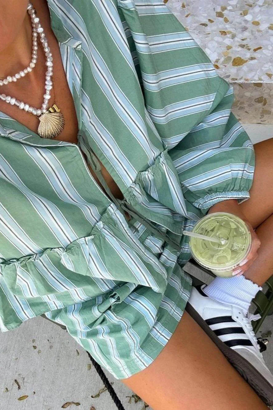 Green - A woman wearing a relaxed-fit, green and white vertically striped two-piece set featuring a tiered peplum top with long balloon sleeves and a tie-front closure, paired with matching loose shorts, standing outdoors.