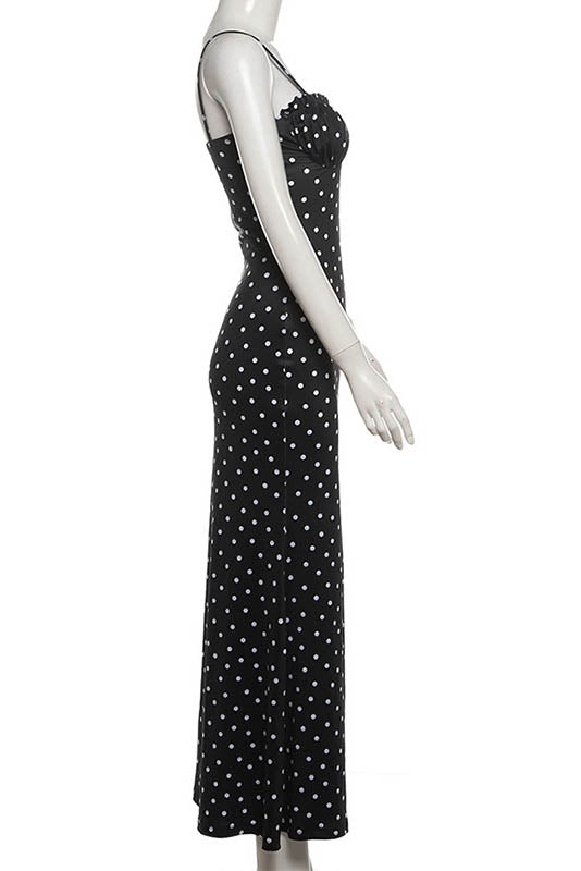 Black - A woman standing by the water wearing a black maxi dress with white polka dots, featuring spaghetti straps and a ruched bodice.