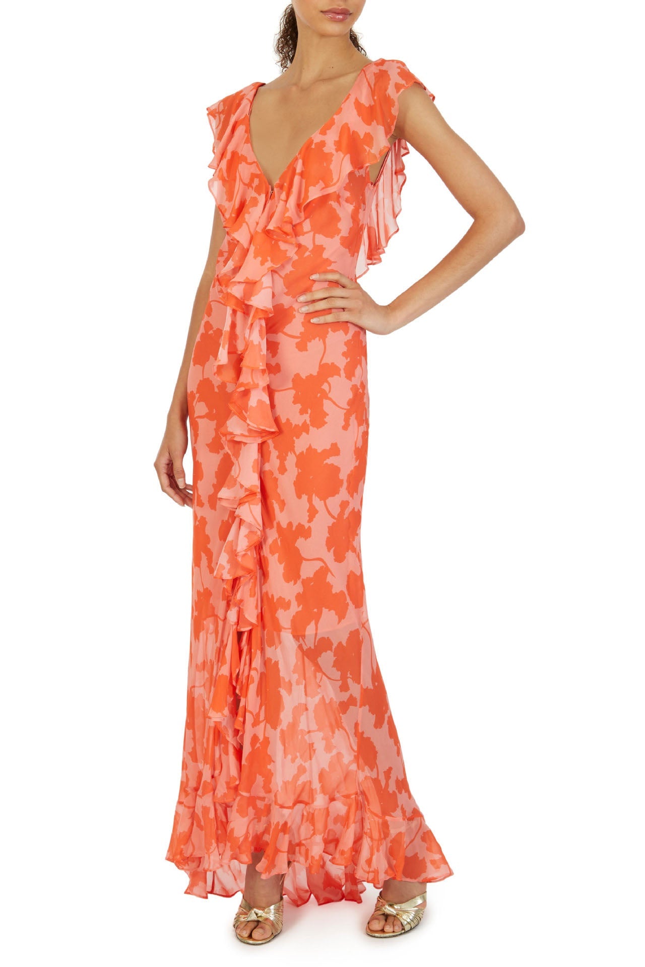 Orange - A woman models an elegant, flowing maxi dress featuring a bold floral print, plunging V-neckline, cascading ruffle details down the front, and a high thigh slit.