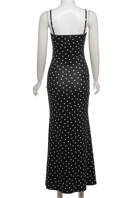 Black - A woman standing by the water wearing a black maxi dress with white polka dots, featuring spaghetti straps and a ruched bodice.
