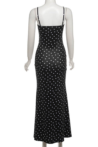 Black - A woman standing by the water wearing a black maxi dress with white polka dots, featuring spaghetti straps and a ruched bodice.