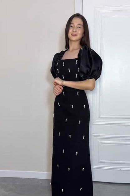 Black - A woman wearing an elegant deep red midi dress featuring large, shiny puff sleeves, a square neckline, and scattered pearl-like embellishments, paired with silver heels and a matching clutch.