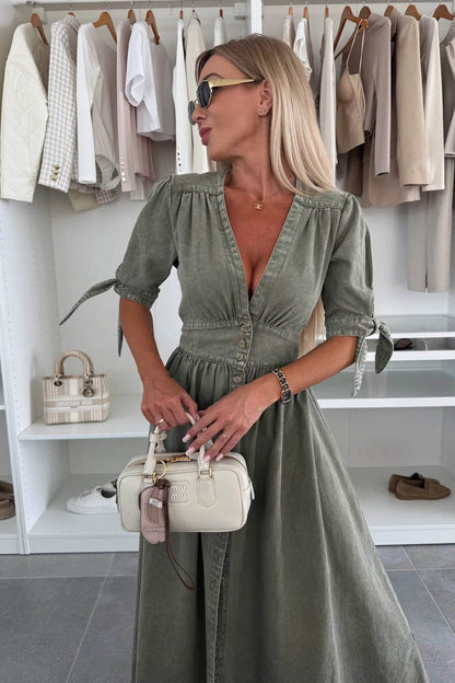Green - Woman wearing a light blue denim-look midi dress with a V-neck, button-down front, and tie-detail short sleeves, styled with trainers and a small white handbag.