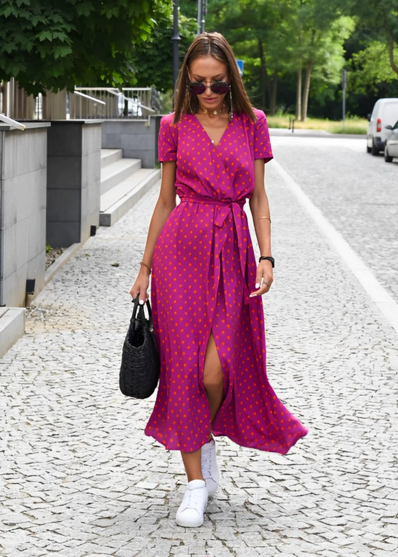 Purple - A woman walking outdoors wearing a vibrant pink and green floral print midi dress with a V-neckline, short sleeves, a tie waist, and a front slit.