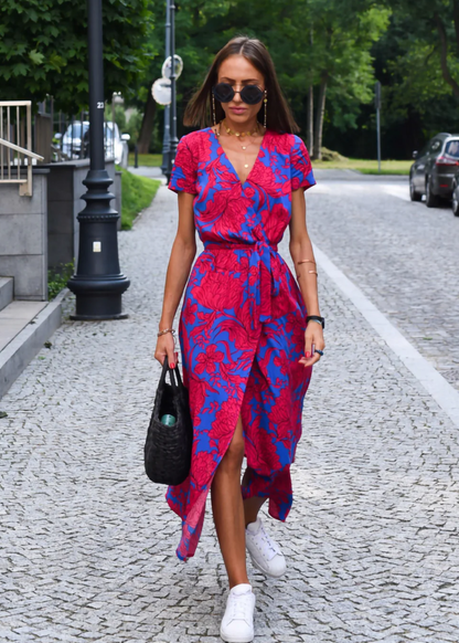 Red and White - A woman walking outdoors wearing a vibrant pink and green floral print midi dress with a V-neckline, short sleeves, a tie waist, and a front slit.