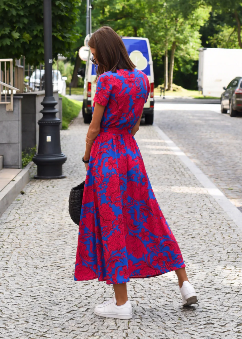 Multicolored - A woman walking outdoors wearing a vibrant pink and green floral print midi dress with a V-neckline, short sleeves, a tie waist, and a front slit.