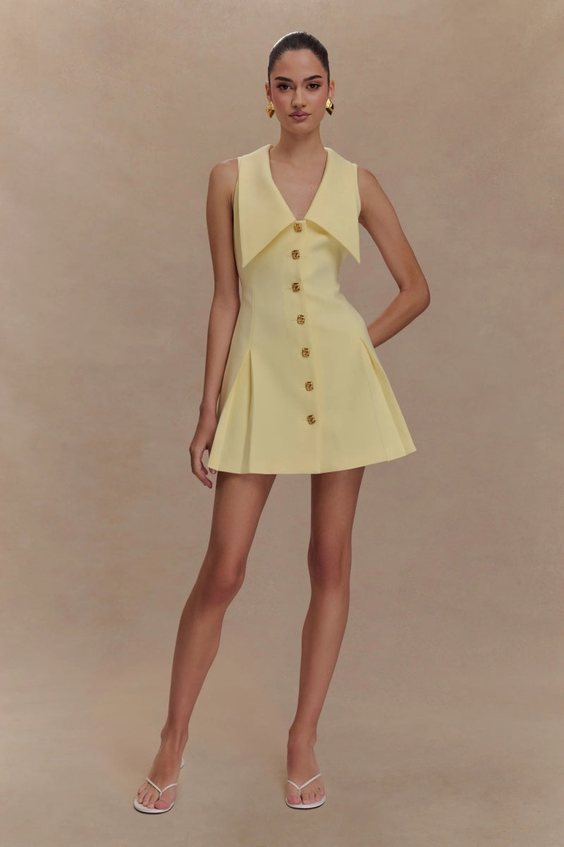 Women's pale yellow sleeveless mini dress featuring an oversized pointed collar, metallic button-down front, and a structured pleated skirt.