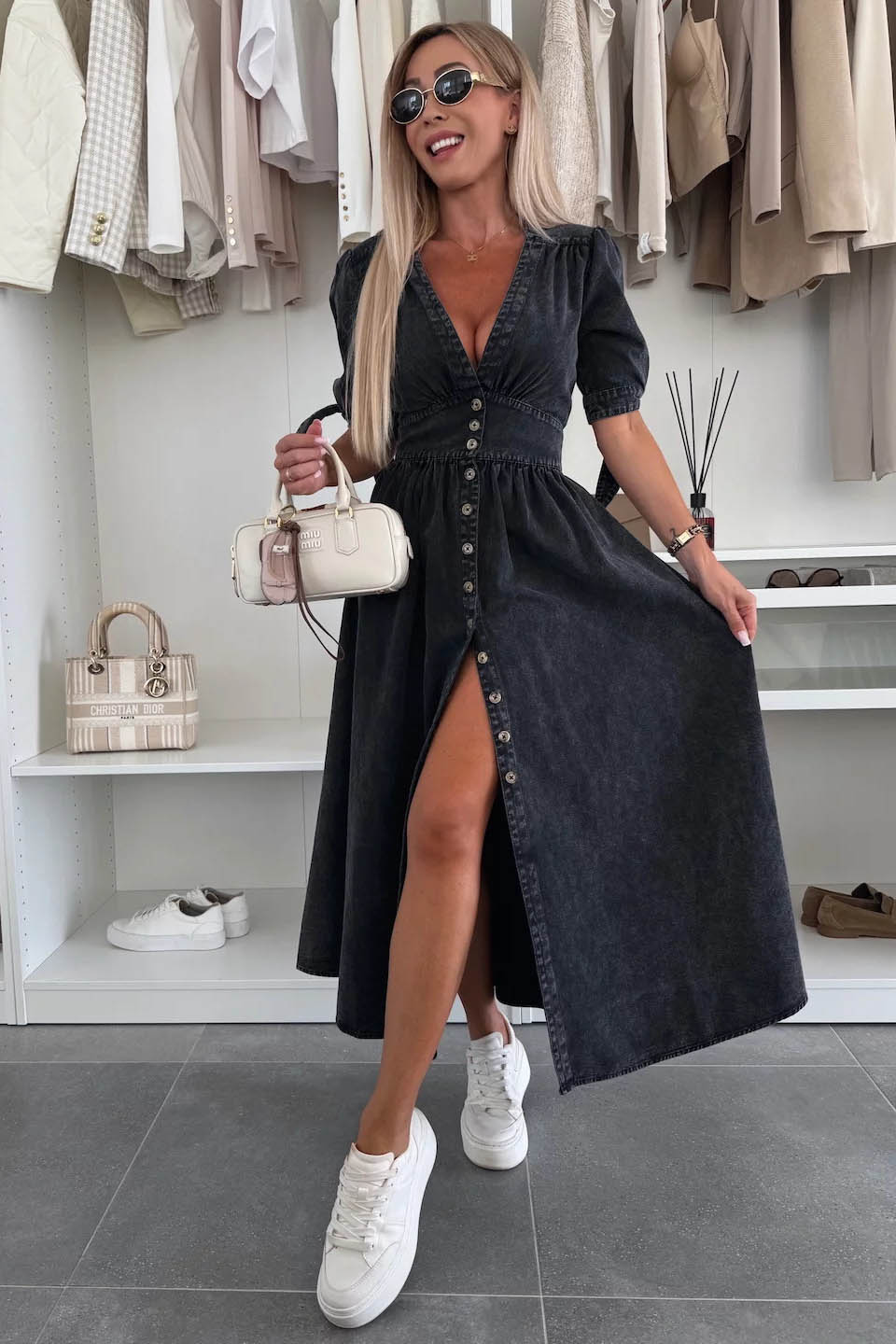 Black - Woman wearing a light blue denim-look midi dress with a V-neck, button-down front, and tie-detail short sleeves, styled with trainers and a small white handbag.