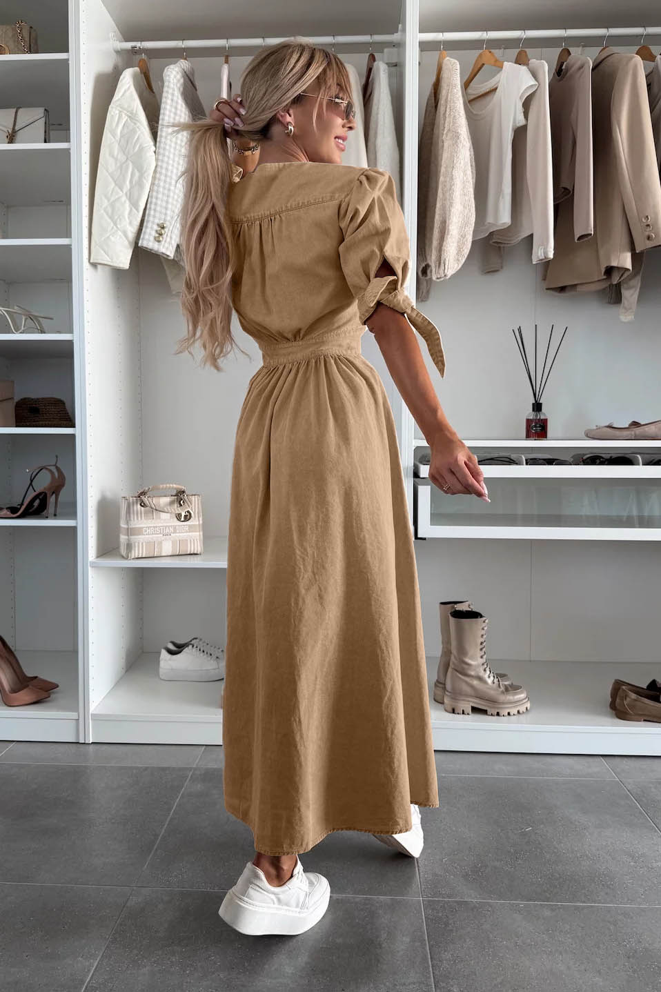 Black - Woman wearing a light blue denim-look midi dress with a V-neck, button-down front, and tie-detail short sleeves, styled with trainers and a small white handbag.
