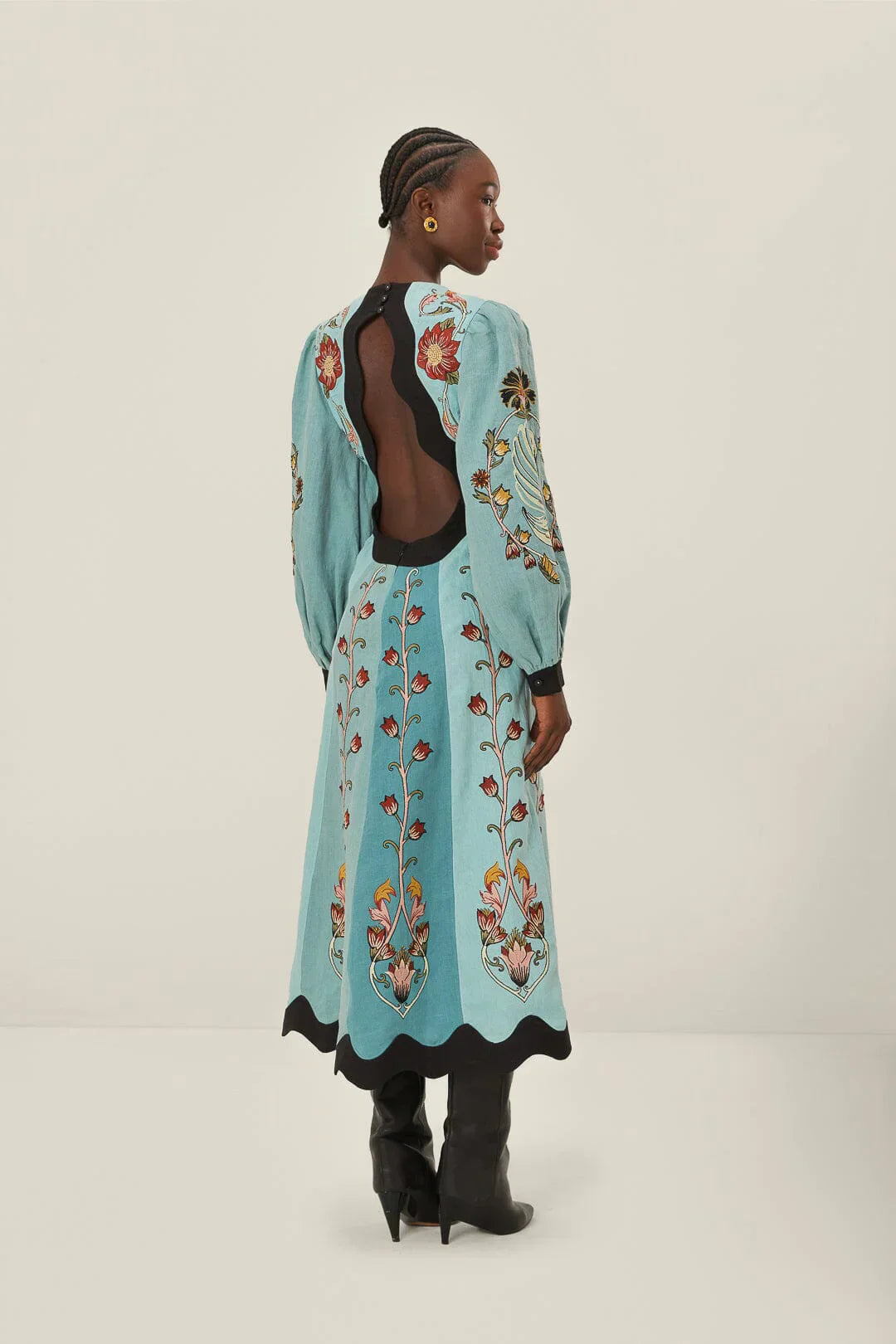 Blue - A woman models a long-sleeve, midi-length dress in shades of blue with a stylized floral print. The dress has a deep V-neckline, voluminous bishop sleeves, and a contrasting black scalloped trim at the neck, cuffs, and hem.