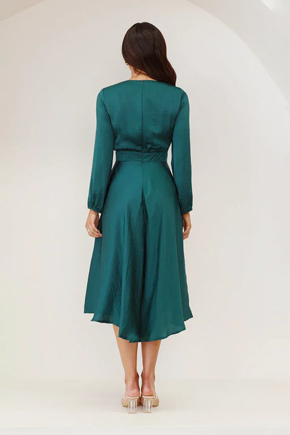 A woman models a long-sleeved, emerald green satin midi dress against a white background. The dress has a deep V-neck with a large tie-front bow, a matching tie-belt at the waist, and an A-line skirt.