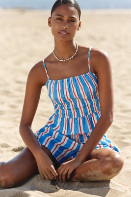 Blue - A woman standing on a sandy beach wearing a matching two-piece set consisting of a shirred peplum cami top and relaxed drawstring shorts, featuring a bold blue, white, and red vertical stripe pattern.