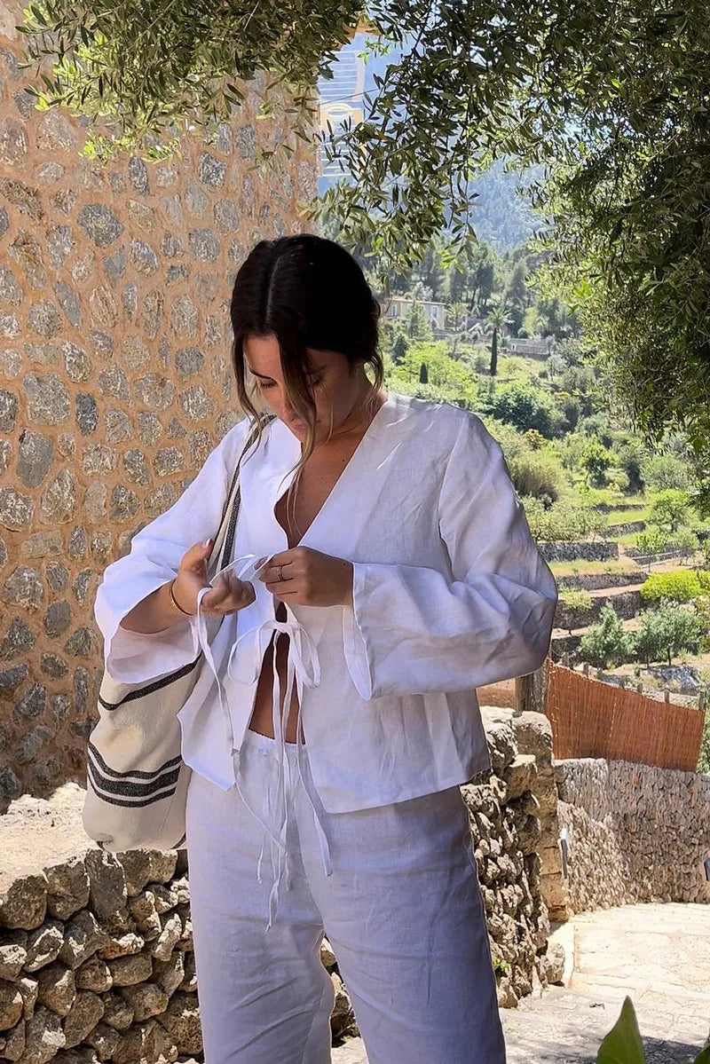 White - Women's white long-sleeve holiday blouse featuring a tie-front closure, V-neckline, and a relaxed, breezy fit, styled with neutral tailored shorts.