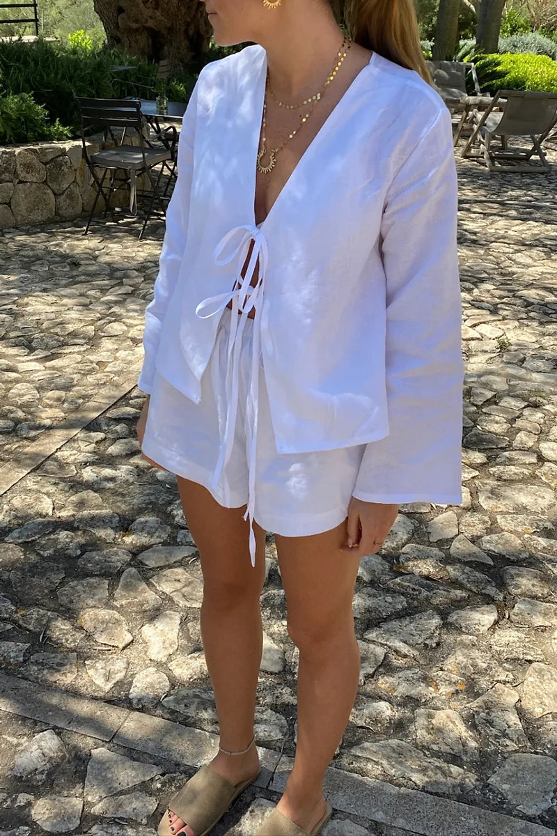 White - Women's white long-sleeve holiday blouse featuring a tie-front closure, V-neckline, and a relaxed, breezy fit, styled with neutral tailored shorts.