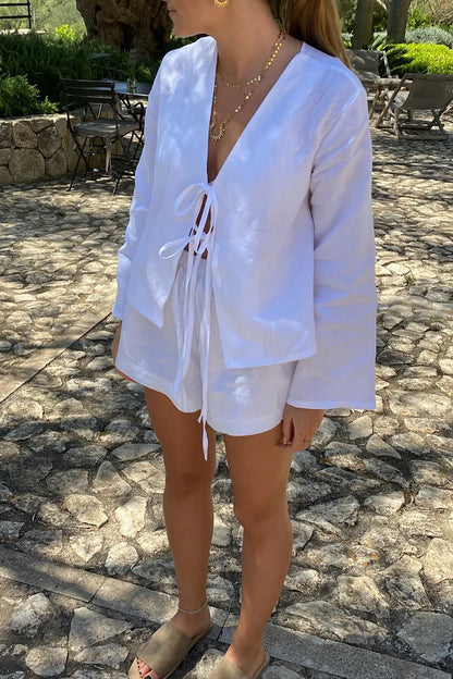 White - Women's white long-sleeve holiday blouse featuring a tie-front closure, V-neckline, and a relaxed, breezy fit, styled with neutral tailored shorts.