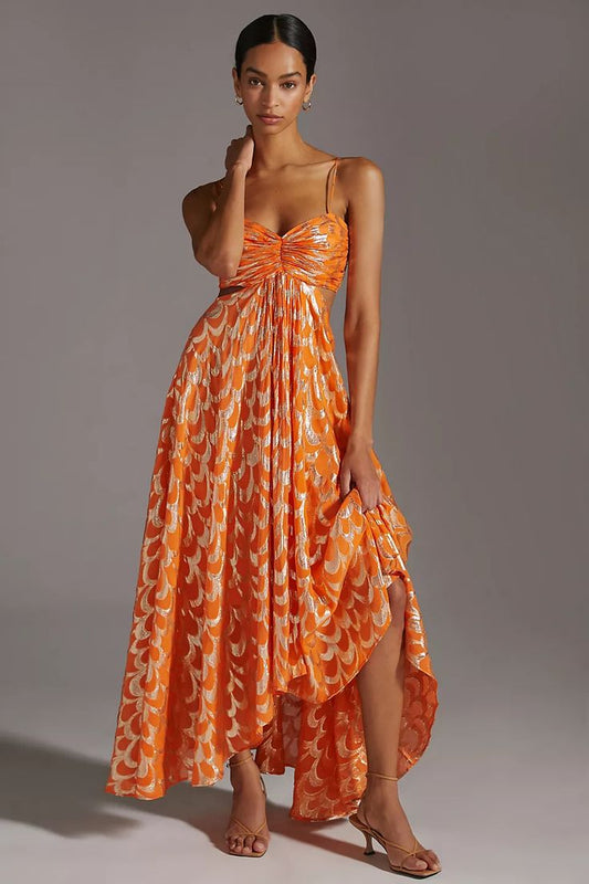 A woman modelling a vibrant orange maxi dress featuring a metallic gold scallop pattern, a ruched sweetheart bodice, side cut-outs, and delicate spaghetti straps.
