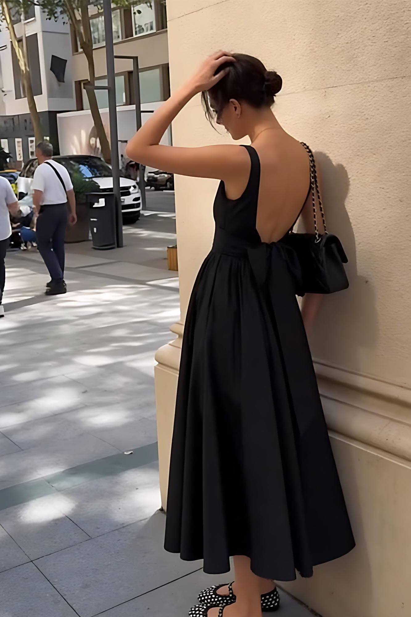 Black - A woman walking outdoors wearing an elegant black sleeveless midi dress featuring a square neckline, fitted bodice, and a full gathered skirt with a dropped waist.