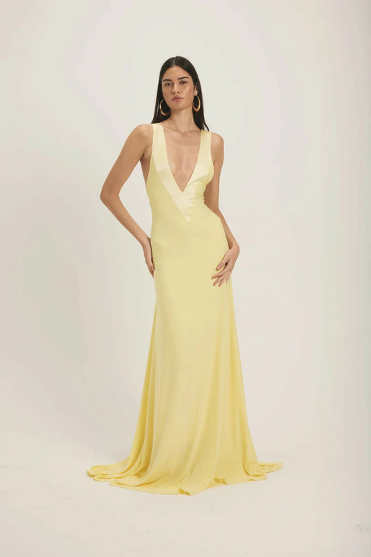 Yellow - A woman modeling a pale yellow, floor-length sleeveless gown featuring a deep plunging V-neckline with a smooth, contrasting trim detail.