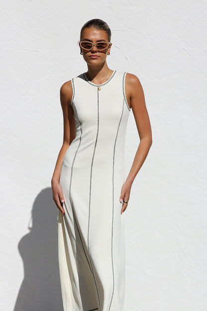 White - A woman stands against a white wall wearing a sleeveless, form-fitting, off-white midi dress. The dress has a high neckline and is detailed with dark vertical contrast stitching along the seams and armholes.