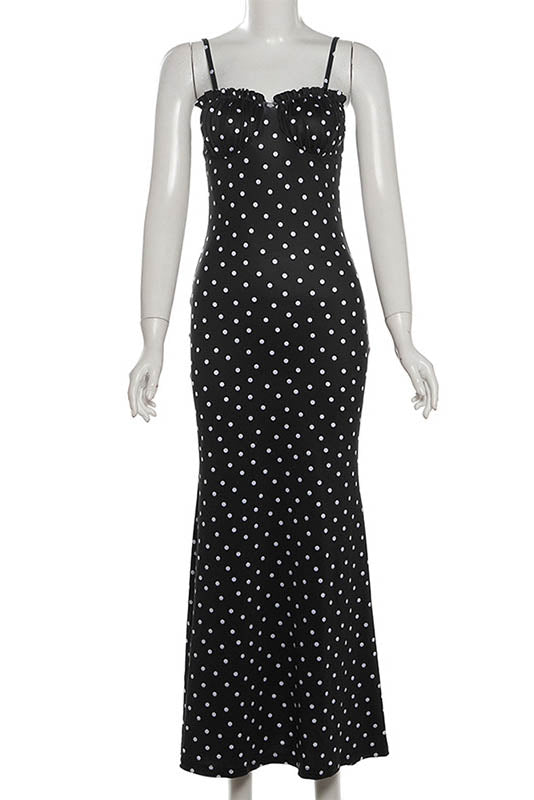 Black - A woman standing by the water wearing a black maxi dress with white polka dots, featuring spaghetti straps and a ruched bodice.