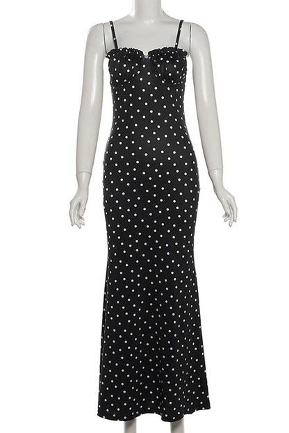 Black - A woman standing by the water wearing a black maxi dress with white polka dots, featuring spaghetti straps and a ruched bodice.