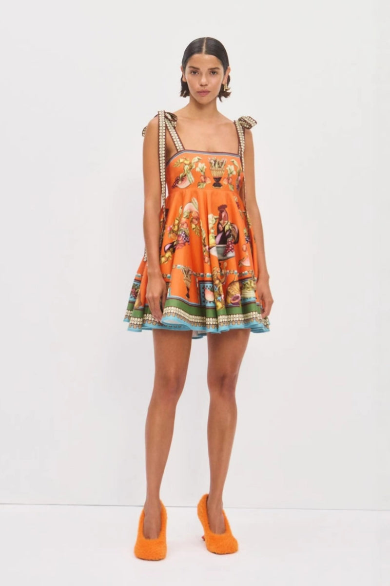 Orange color - Women's vibrant mini dress featuring a square neckline, tie-shoulder straps, a flared skirt, and an ornate still-life and fruit print with a contrast border hem.