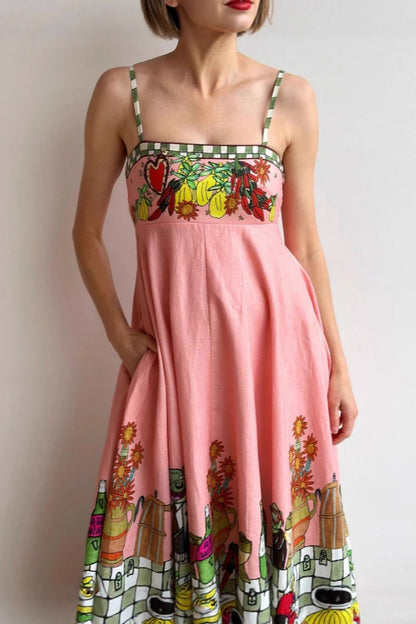 Pink - A model wearing a pink strappy A-line midi dress featuring a vibrant, illustrative novelty print of a dining table, hearts, and checkered borders.