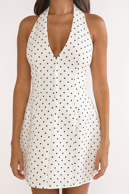 White - A woman wearing a white mini dress with black polka dots, featuring a plunging halter neckline and a structured, tailored fit.