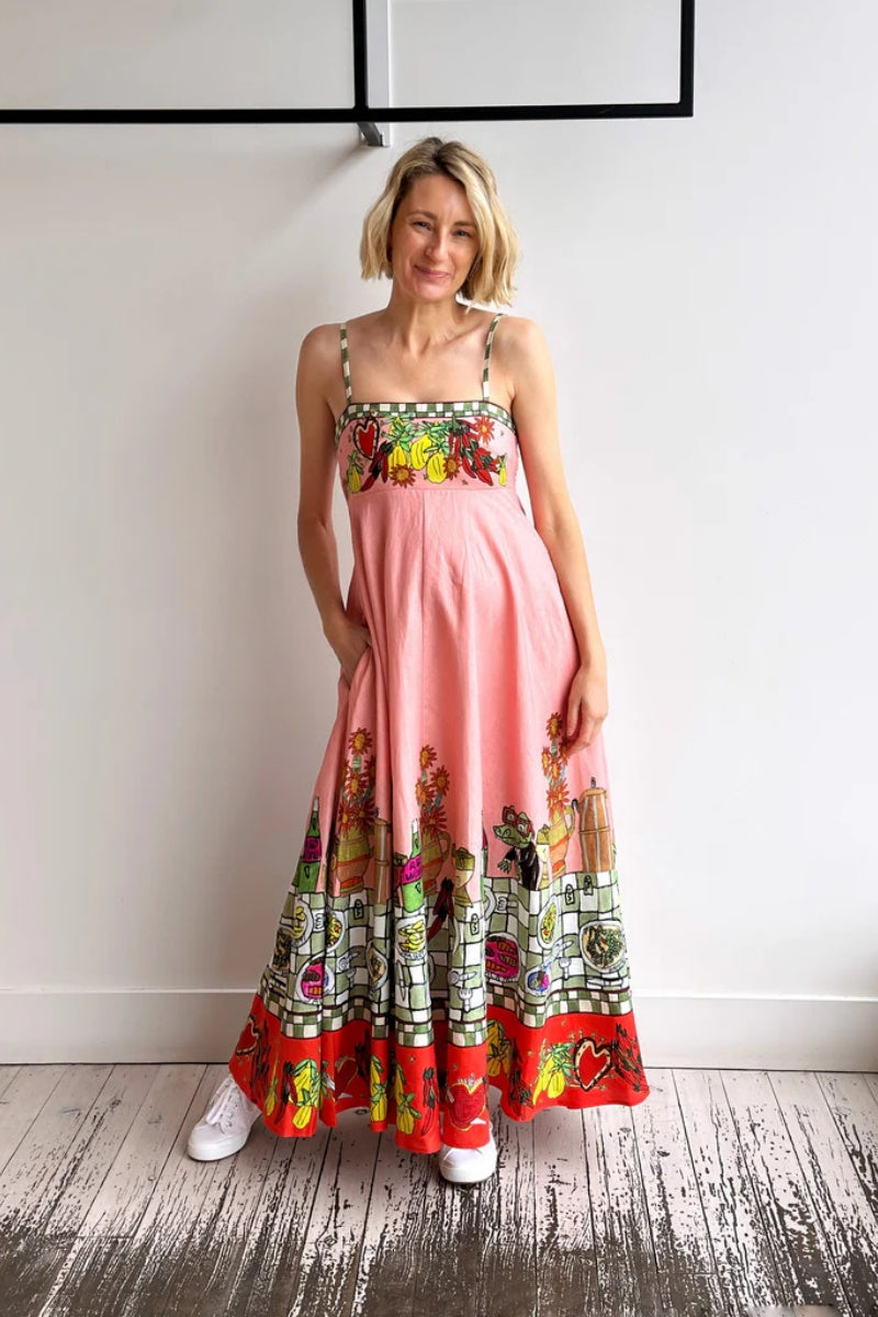 Pink - A model wearing a pink strappy A-line midi dress featuring a vibrant, illustrative novelty print of a dining table, hearts, and checkered borders.