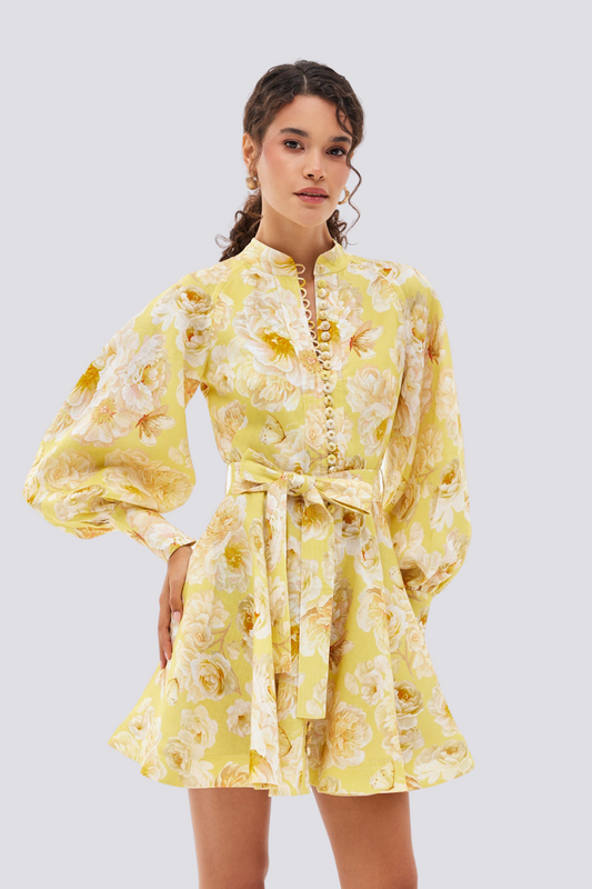 Yellow - A woman wearing a yellow mini dress with a large white floral print, featuring long balloon sleeves, a high neckline with button detailing, and a waist tie belt.