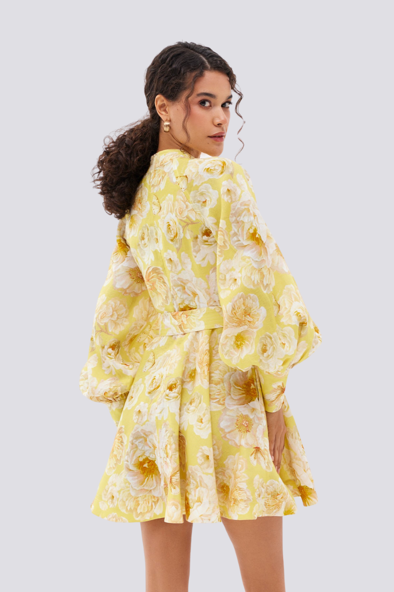 Yellow - A woman wearing a yellow mini dress with a large white floral print, featuring long balloon sleeves, a high neckline with button detailing, and a waist tie belt.