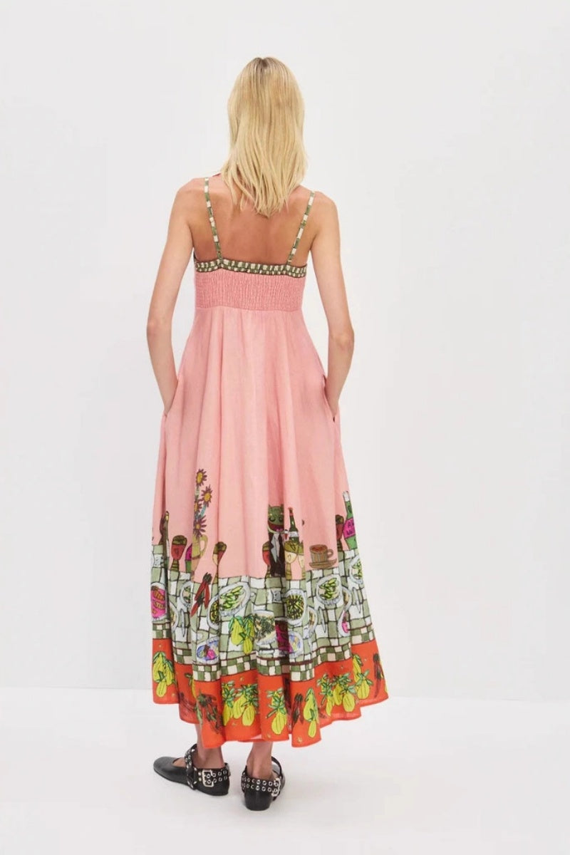 Pink - A model wearing a pink strappy A-line midi dress featuring a vibrant, illustrative novelty print of a dining table, hearts, and checkered borders.