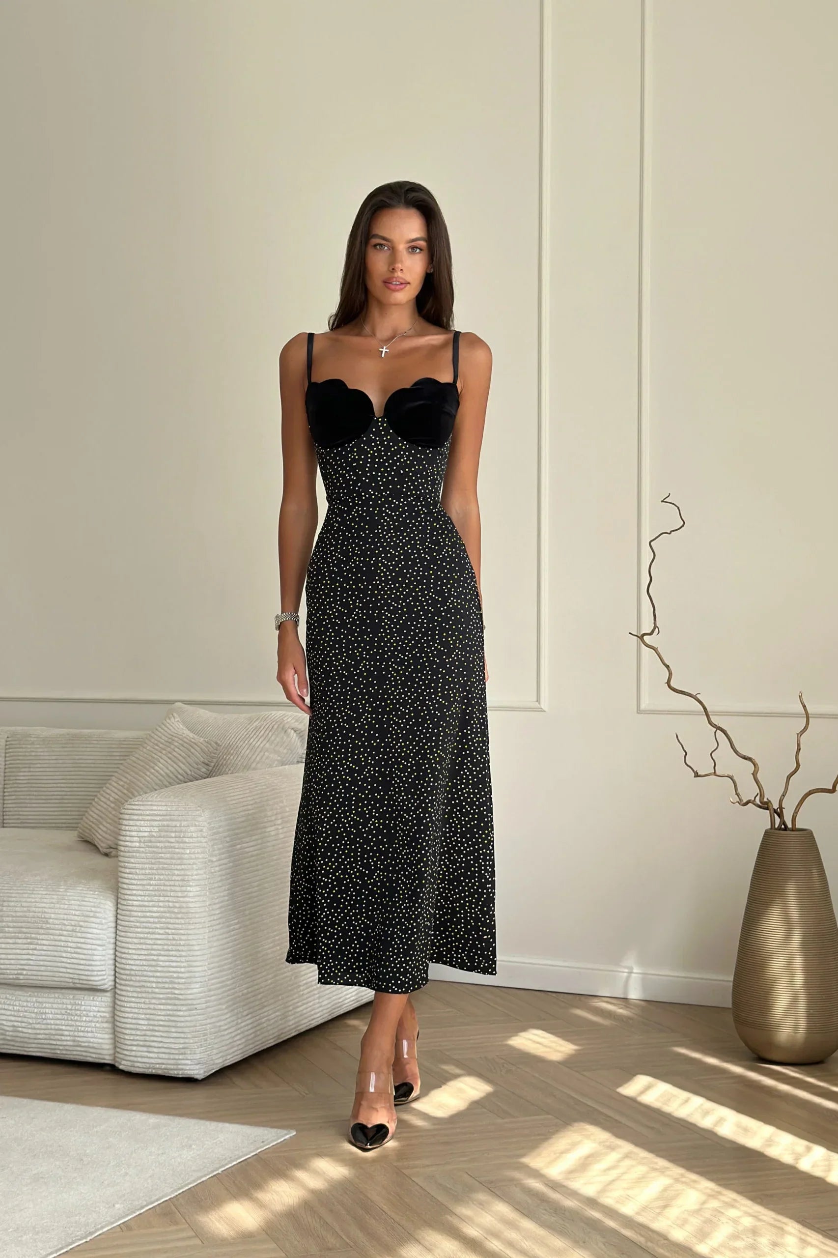 Black - Woman leaning against a white wall wearing a black maxi dress with a solid sweetheart bustier top and white polka dot patterned skirt.