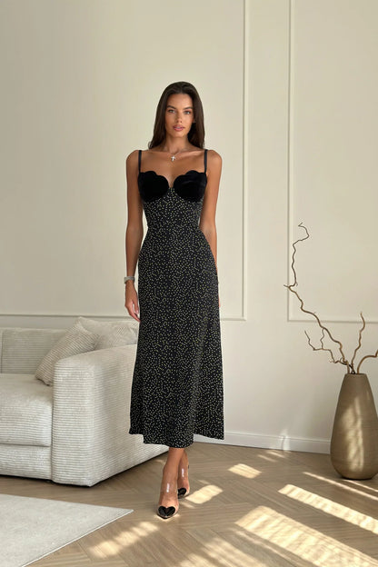 Black - Woman leaning against a white wall wearing a black maxi dress with a solid sweetheart bustier top and white polka dot patterned skirt.