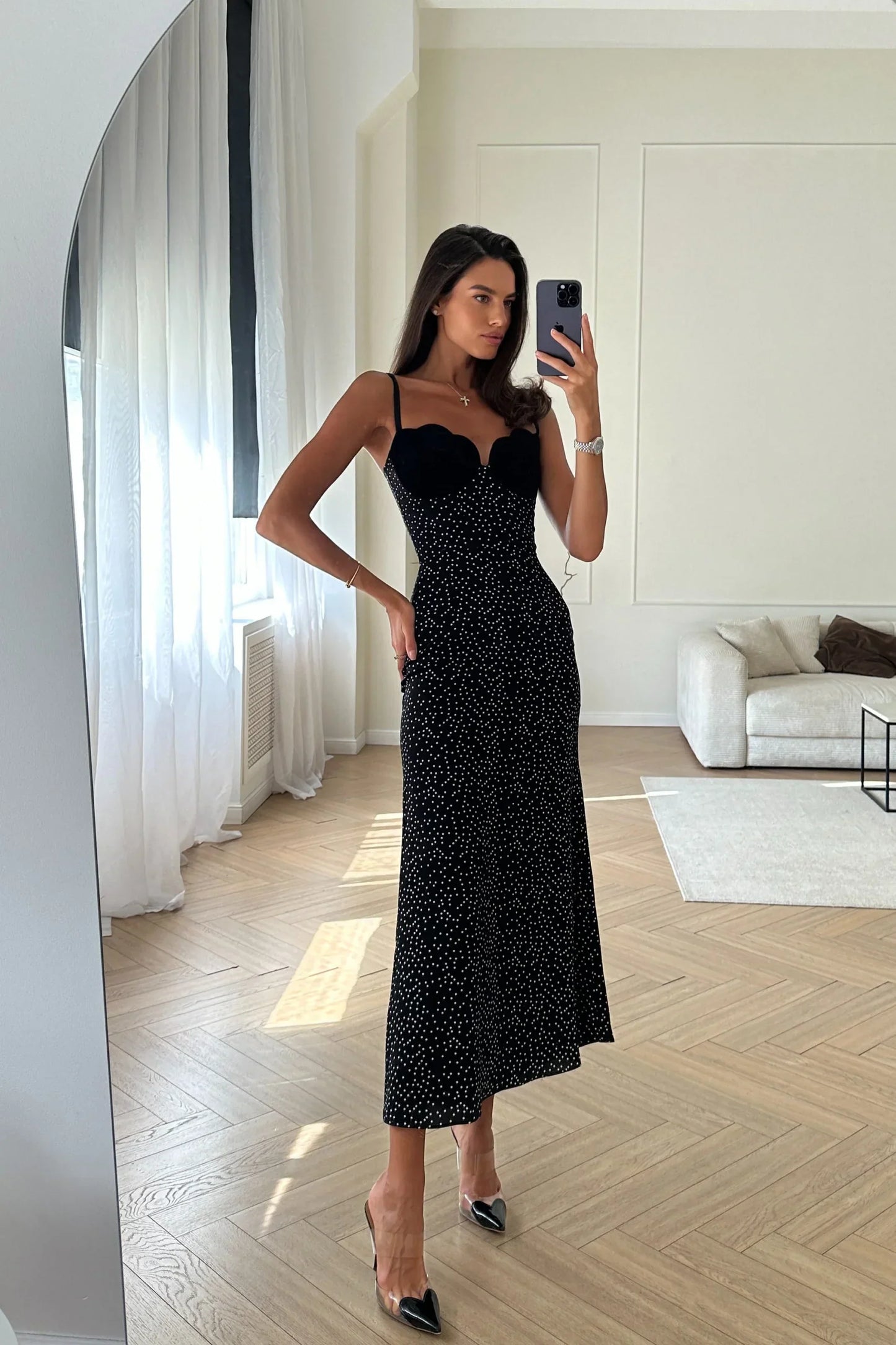 Black - Woman leaning against a white wall wearing a black maxi dress with a solid sweetheart bustier top and white polka dot patterned skirt.