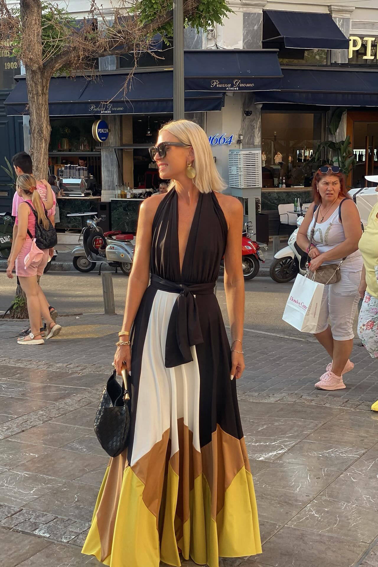 Multi - Women wearing an elegant halter neck maxi dress featuring a plunging neckline, wide tie-waist belt, and a flowing A-line skirt with bold black, white, brown, and mustard colour-block panels.