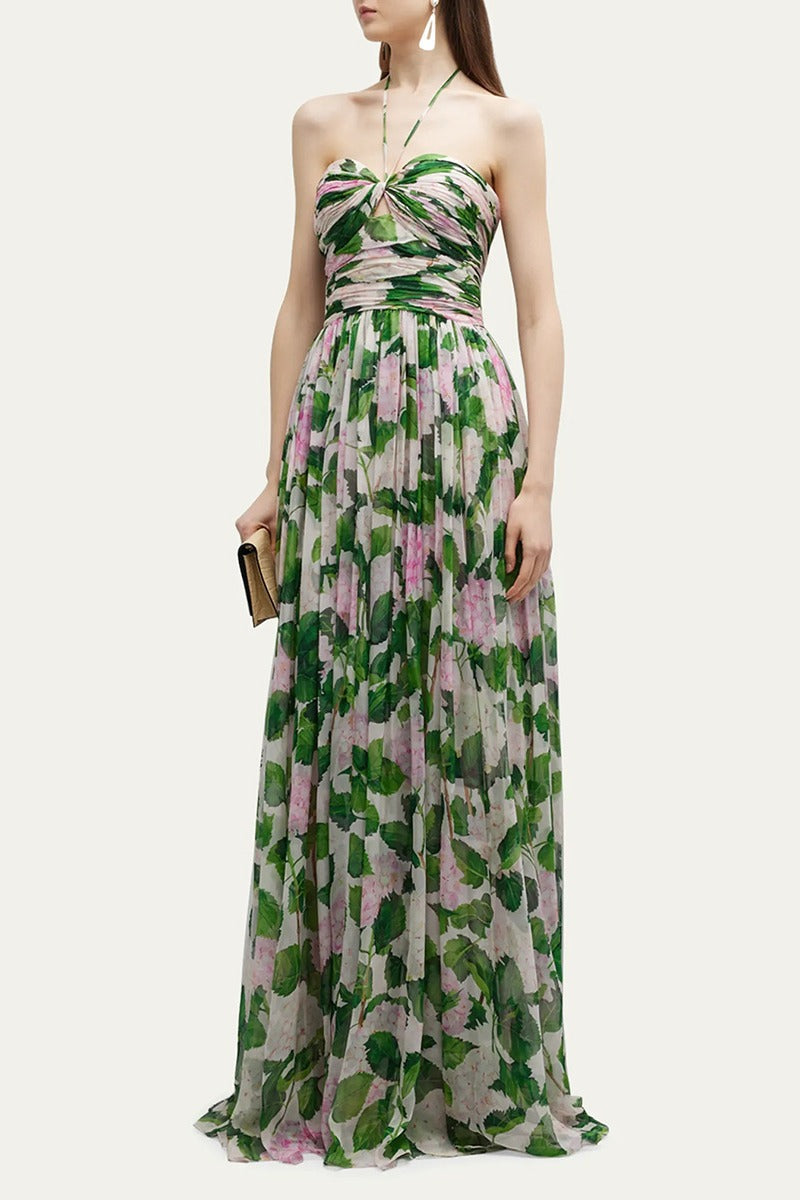 Green - A woman modelling a flowing maxi dress with a ruched halterneck bodice and a large pink and green botanical floral print.