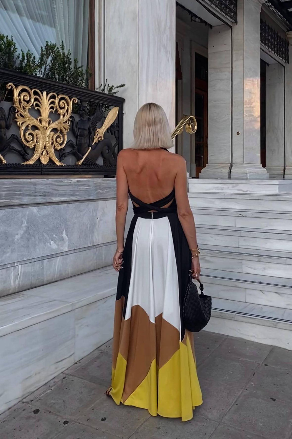 Multi - Women wearing an elegant halter neck maxi dress featuring a plunging neckline, wide tie-waist belt, and a flowing A-line skirt with bold black, white, brown, and mustard colour-block panels.