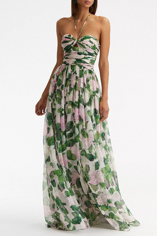 A woman modelling a flowing maxi dress with a ruched halterneck bodice and a large pink and green botanical floral print.