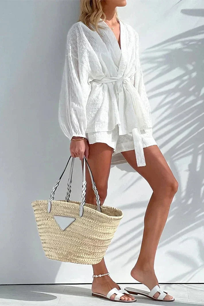White - Woman wearing a white, lightweight wrap blouse featuring a textured dobby pattern, voluminous long sleeves, and a tie waist belt.