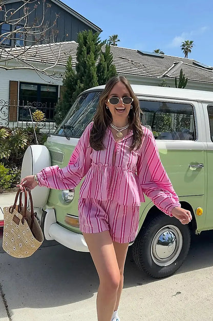 Pink - A woman wearing a relaxed-fit, green and white vertically striped two-piece set featuring a tiered peplum top with long balloon sleeves and a tie-front closure, paired with matching loose shorts, standing outdoors.