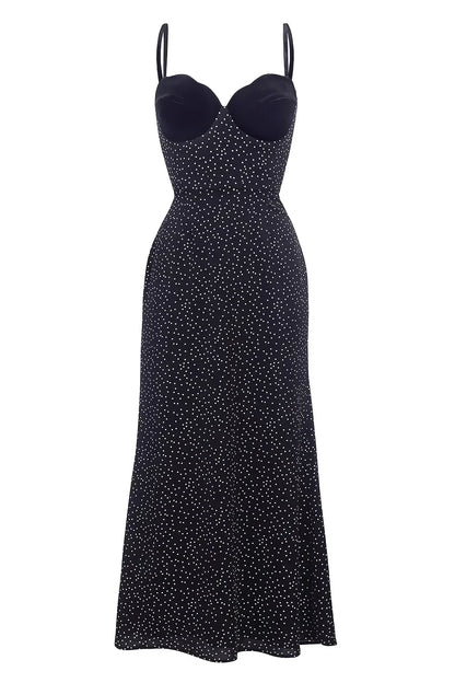 Black - Woman leaning against a white wall wearing a black maxi dress with a solid sweetheart bustier top and white polka dot patterned skirt.