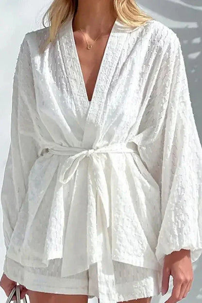 White - Woman wearing a white, lightweight wrap blouse featuring a textured dobby pattern, voluminous long sleeves, and a tie waist belt.