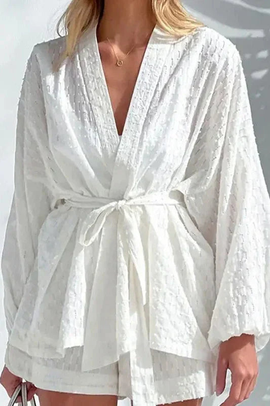 White - Woman wearing a white, lightweight wrap blouse featuring a textured dobby pattern, voluminous long sleeves, and a tie waist belt.