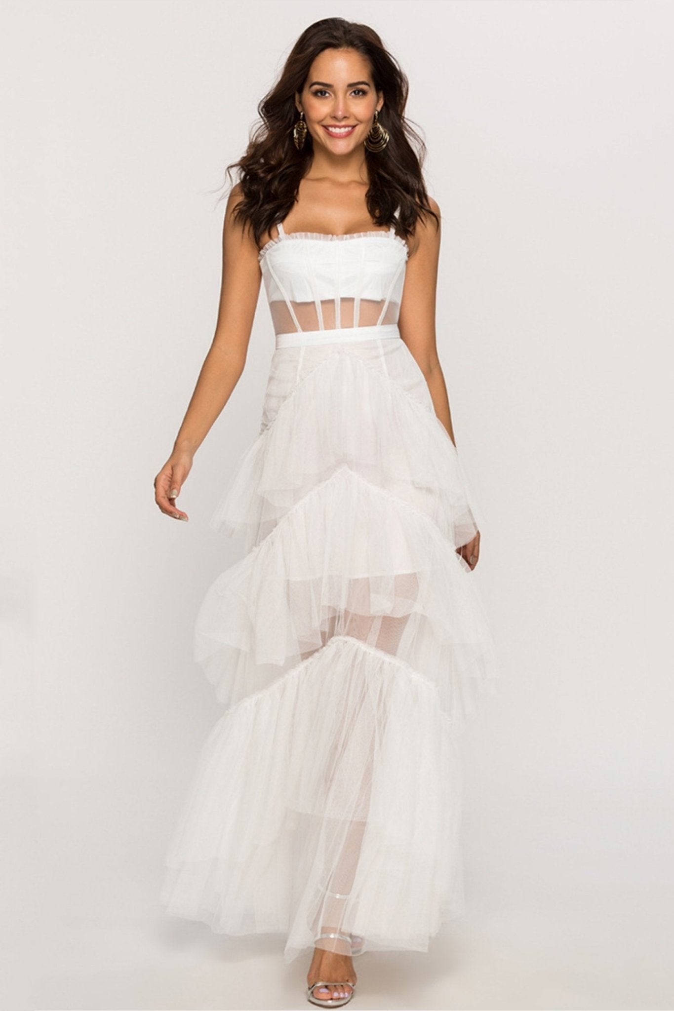 Pink - A woman wearing a pale pink, floor-length maxi dress featuring a structured corset-style bodice with sheer panels and a voluminous, multi-tiered tulle skirt.
