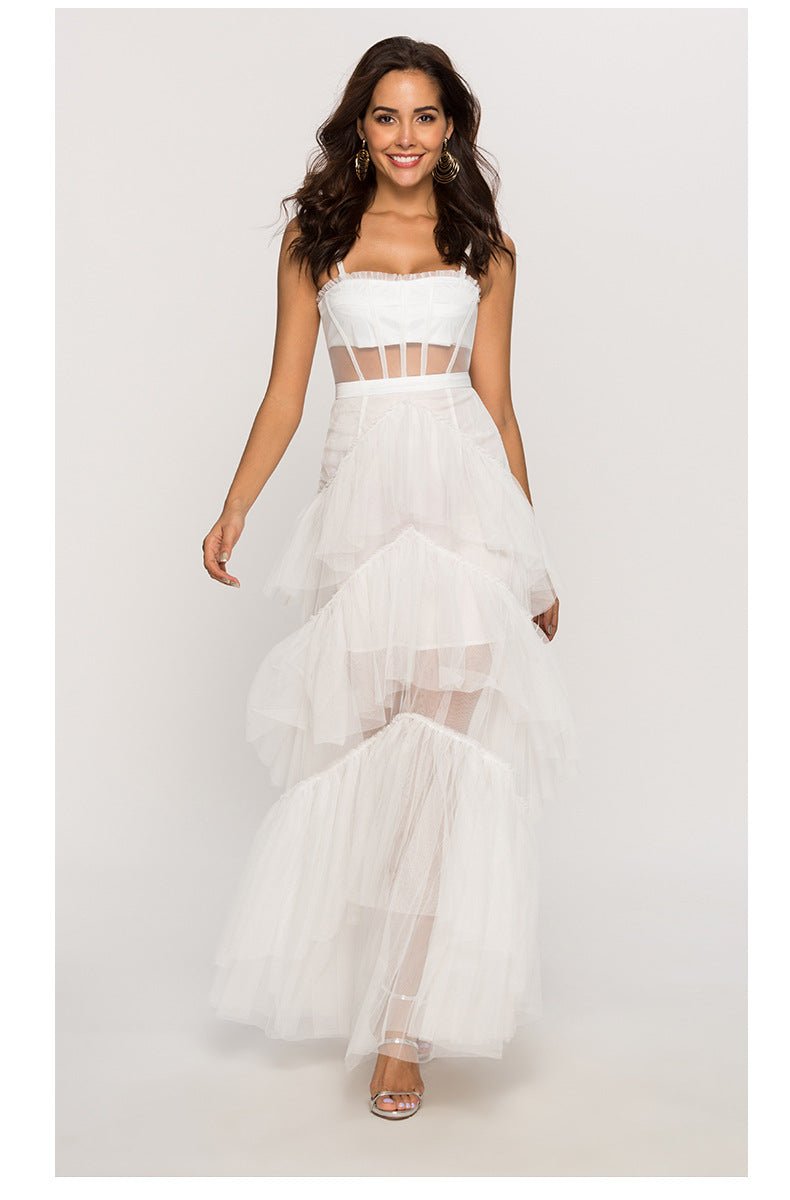 White - A woman wearing a pale pink, floor-length maxi dress featuring a structured corset-style bodice with sheer panels and a voluminous, multi-tiered tulle skirt.