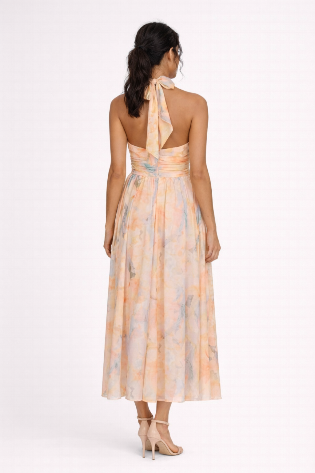 Peach - A model wearing a sleeveless floral halter-neck midi dress with a wide ruched waistband and flowing A-line skirt.