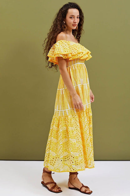 Yellow - A woman wearing a yellow and white off-the-shoulder midi dress featuring a smocked bodice, ruffled neckline, tiered skirt, and intricate broderie anglaise cut-out patterns.